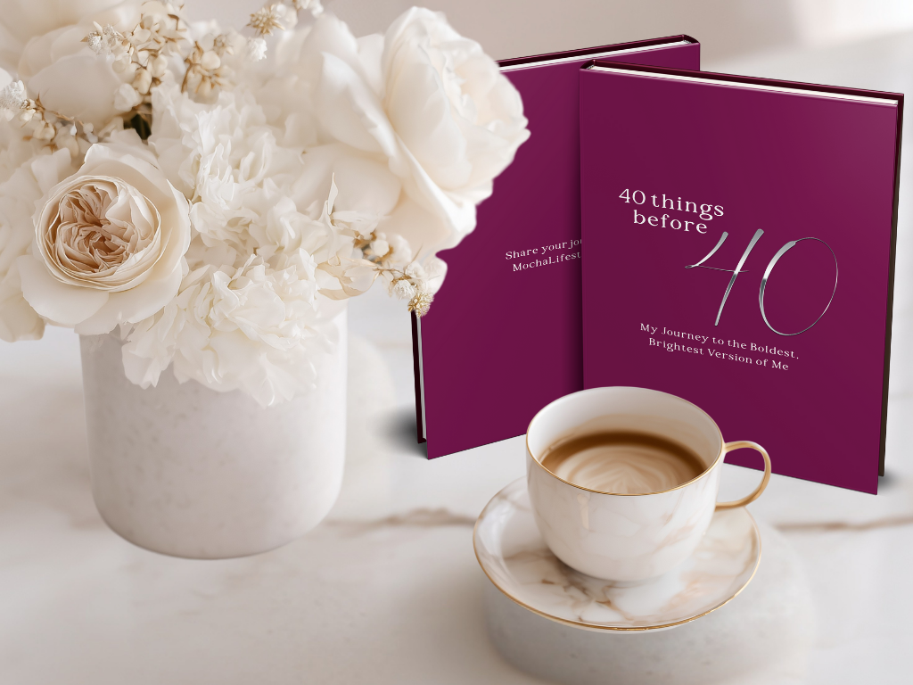 Closed journal titled '40 Things Before 40' with a cup of coffee and flowers on a table.