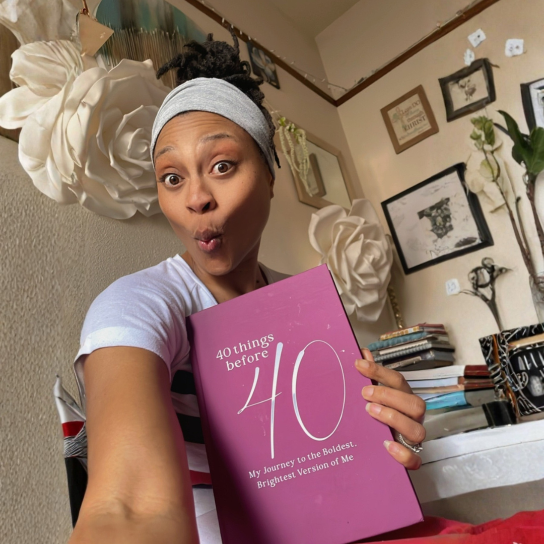 Person holding a pink book titled '40 Things Before 40' in a room with decor.